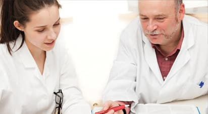 年轻女性整骨疗法的医科学生在白大褂的监护下一位经验丰富的医生是谁拿着红笔。