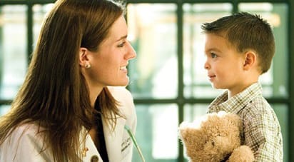 Image of ATSU student doctor talking to a little boy patient who is holding a Teddy Bear.